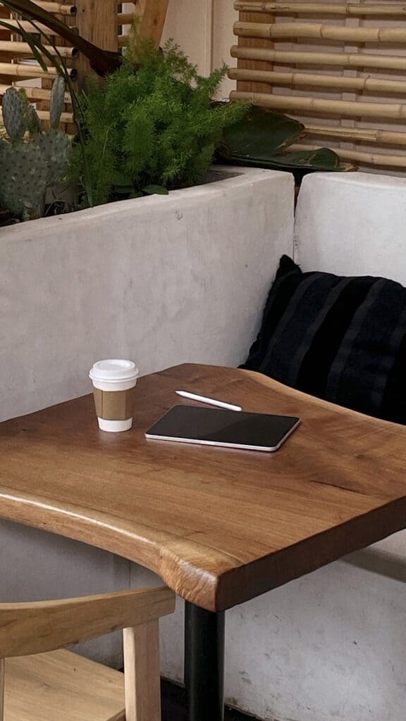 Table with a black notebook, white pen and coffee cup sitting on it.